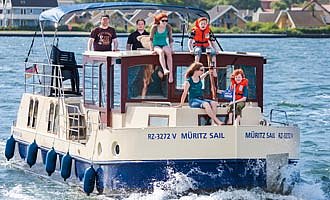 unser Hausboot Primus Kormoran 1280 auf der Müritz vor dem Hafendorf Müritz mit einer Familie an Deck