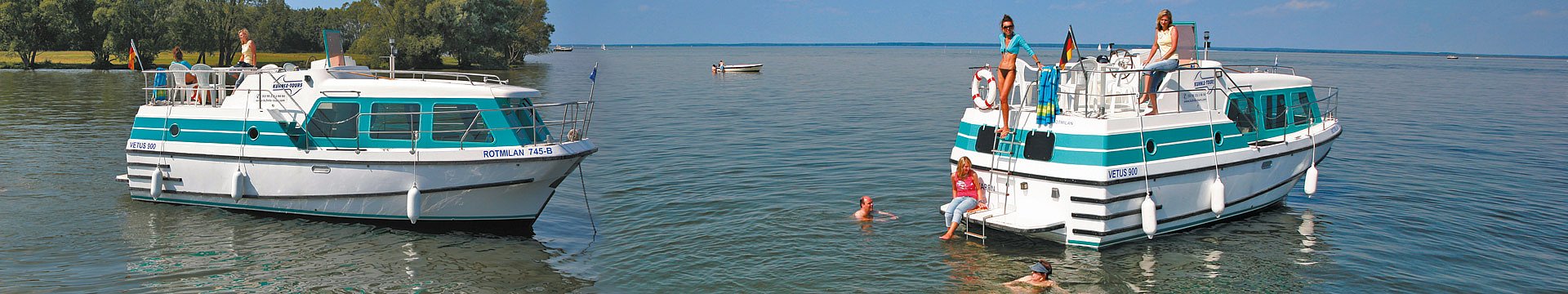 Zwei Vetusboote ankern auf einem See. Einige Menschen baden, andere sitzen oder stehen bequem an Bord.