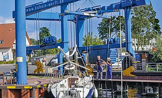 Mit einem Travellift wird ein Boot zu Wasser gelassen.